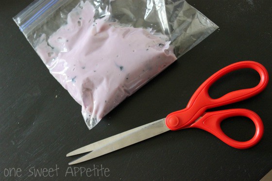 zip top bag filled with blueberry yogurt on w black table with a pair of red scissors sitting next to the bag