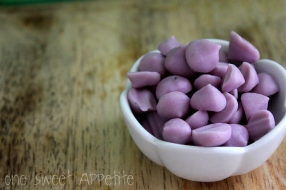 small white bowl sitting on a light brown wooden table filled with purple colored frozen yogurt pieces