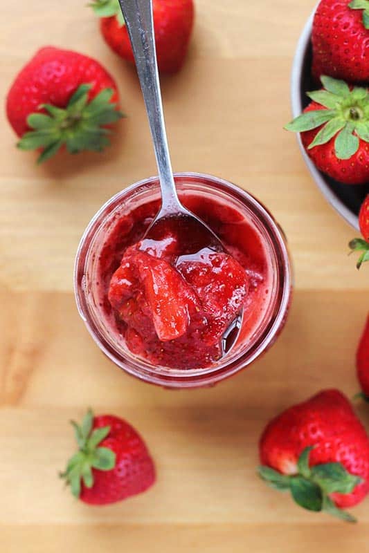 top down image of a mason jar filled with strawberry sauce on a spoon