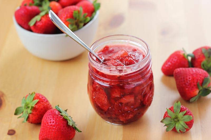 mason jar filled with berry sauce and surrounded by fresh berries