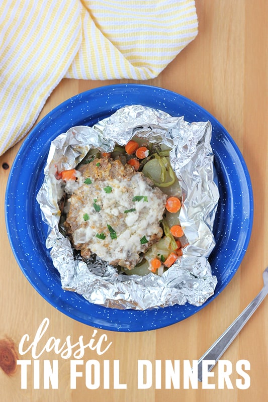 top down image showing a blue camping plate with a foil packet filled with sliced potatoes, carrots, green beans and a burger patty 