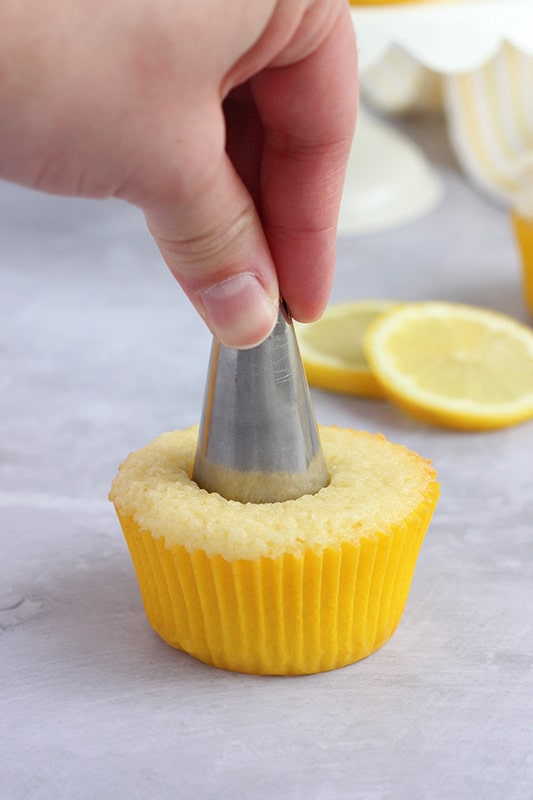 baked cupcake in a yellow cupcake liner with a metal piping tip being pushed into the center