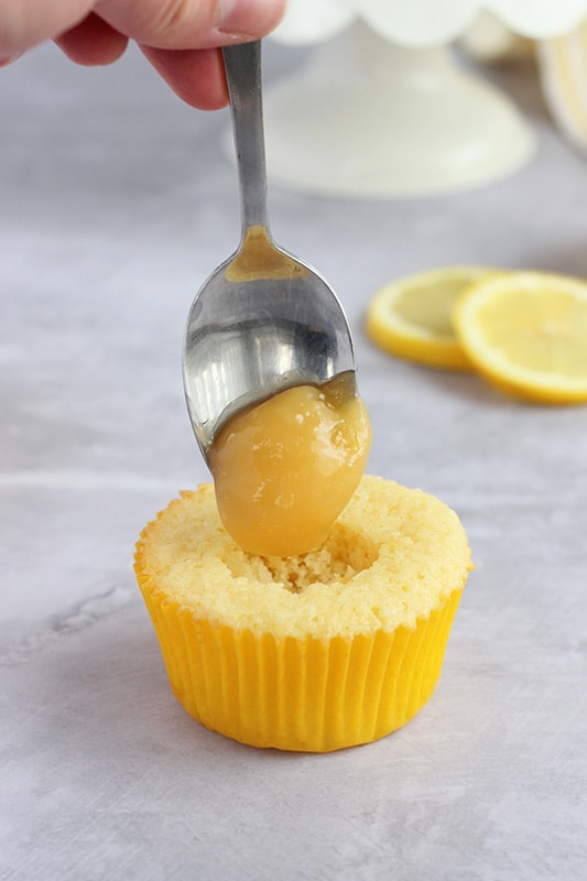 baked cupcake with the center cut out with a spoon spooning lemon curd into the center