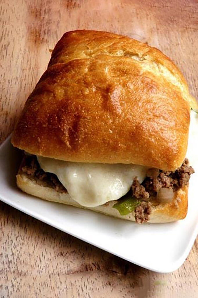 close up image of a sloppy joe on a white plate sitting on a wooden backdrop