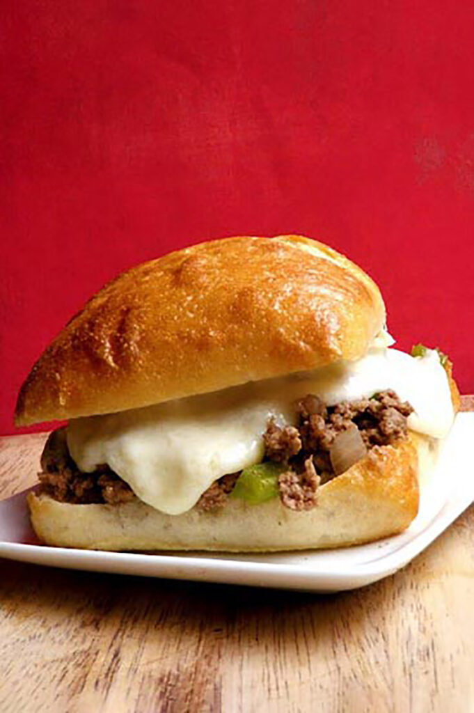 sloppy joe sitting on a white plate with cheese melting down the side with a red background