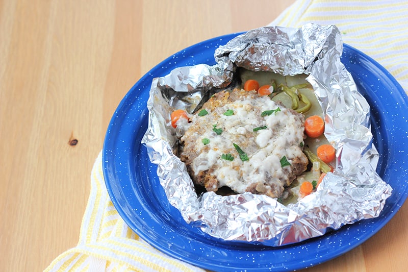 tin foil shaped like a bowl filled with sliced potatoes, carrots, and a beef patty that is topped with mushroom soup