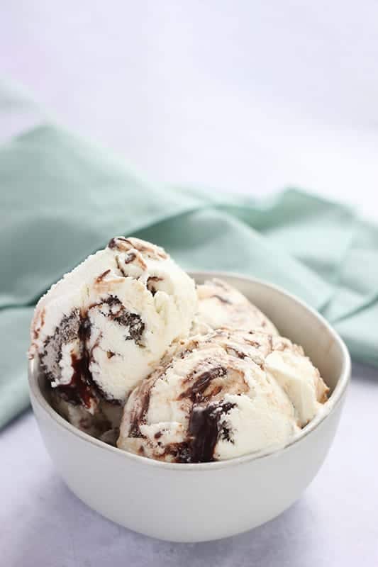 off white small bowl with three scoops of chocolate swirled ice cream sitting inside. A light blue napkin sitting off to the side.
