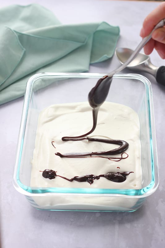 spoon drizzling fudge over the top of vanilla ice cream 