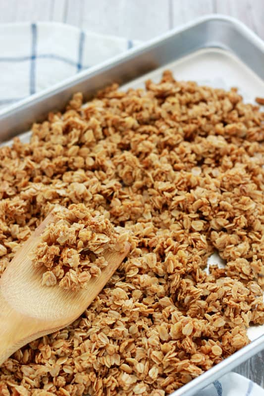 Homemade granola on a baking tray with a wooden spoon