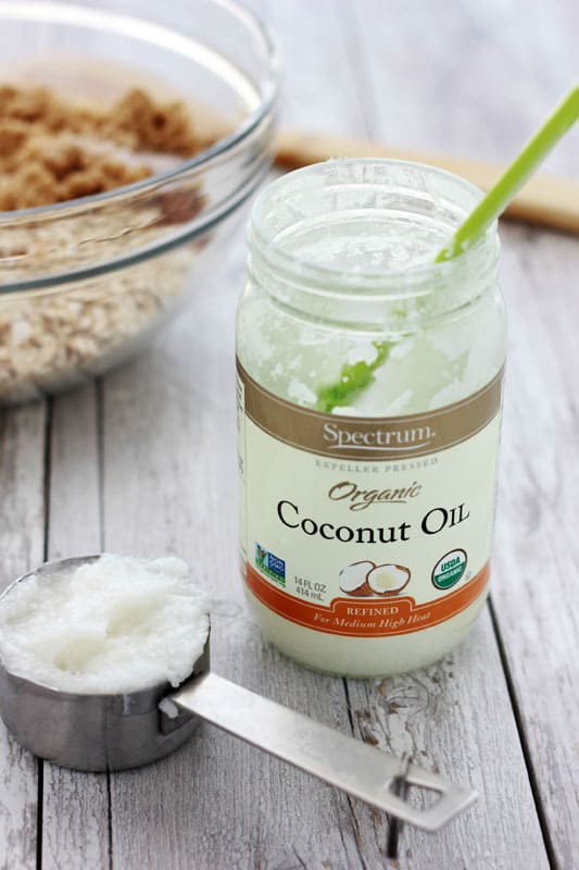 a jar of coconut oil sitting on a white wooden tabletop and a measuring cup filled with oil