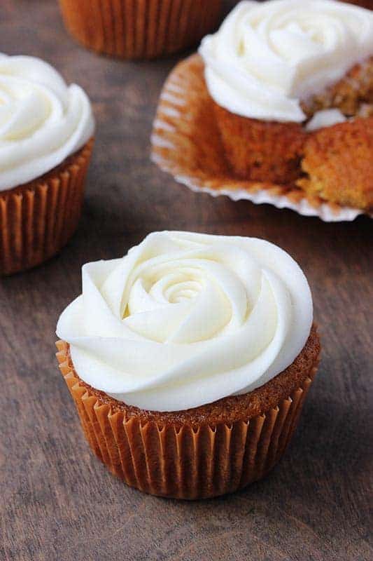Single cupcake in a brown wrapper topped with white frosting that is piped to look like a rose. 