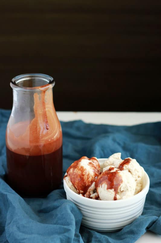 bowl of ice cream topped with chocolate syrup with a jar sitting next to the bowl with more syrup on a blue napkin