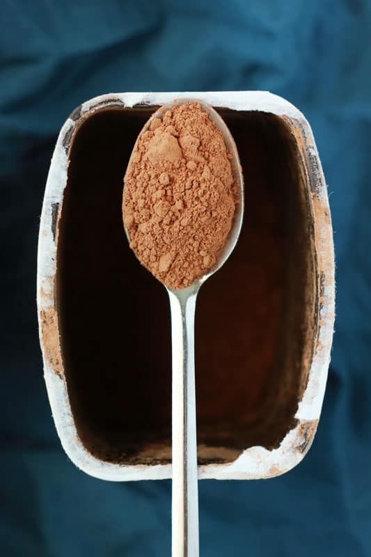 spoon holding cocoa powder over an open container of cocoa powder