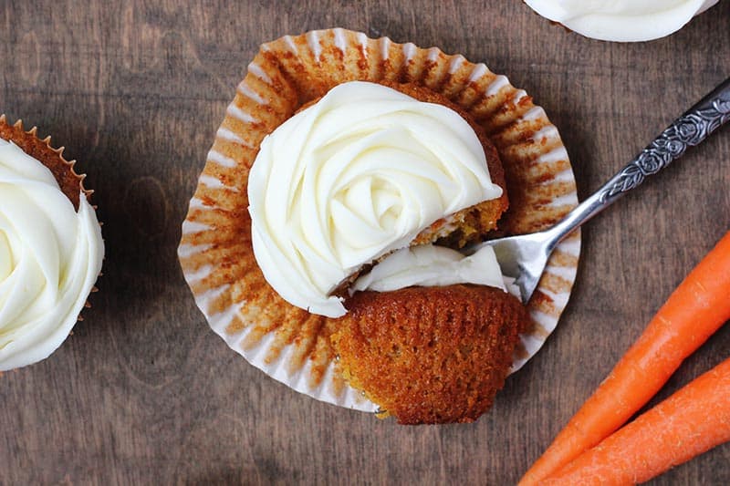 carrot cupcake sitting on top of an open wrapper with a bite sitting on a fork