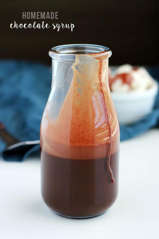 glass milk jar filled with chocolate sauce with a drip going down the side on a white table top with a blue napkin sitting in the background
