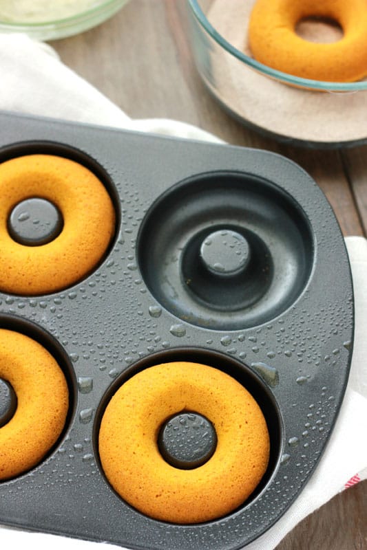 donut tin with fresh baked donuts sitting inside on a wooden tabletop with a white napkin