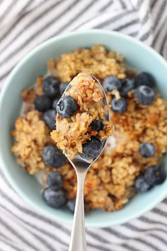 a spoon filled with oats and blueberries over a bowl of baked oatmeal