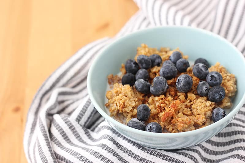 a bowl of baked oatmeal on a wooden table topped with fresh blueberries