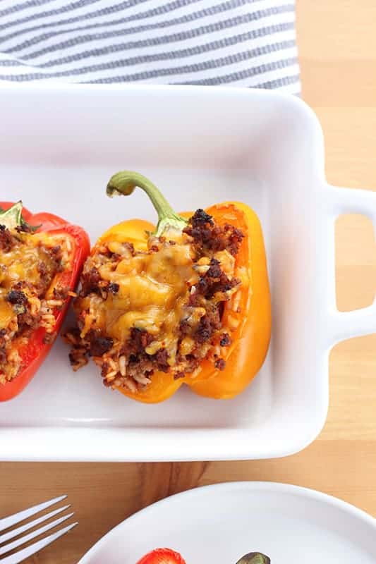 white casserole dish with handles sitting on a wooden table top with a yellow and red stuffed pepper sitting in the center