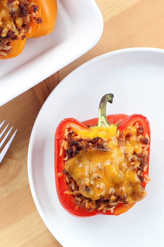 single red pepper that is stuffed with beef, rice, and sauce topped with cheese sitting on a white plate on top of a wooden table top