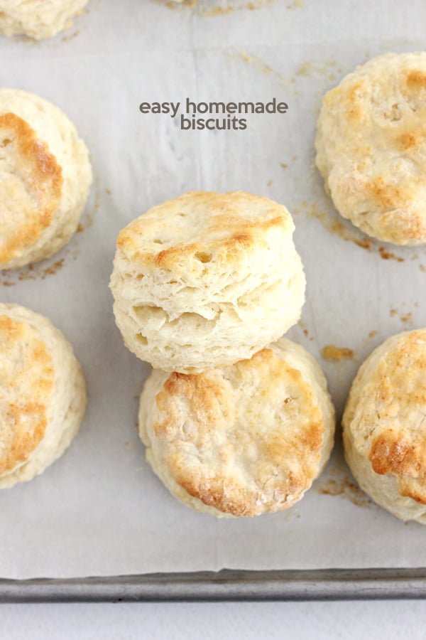 baking tray lined with parchment paper and golden brown biscuits, with two biscuits leaning onto each other to show off the flaky layers
