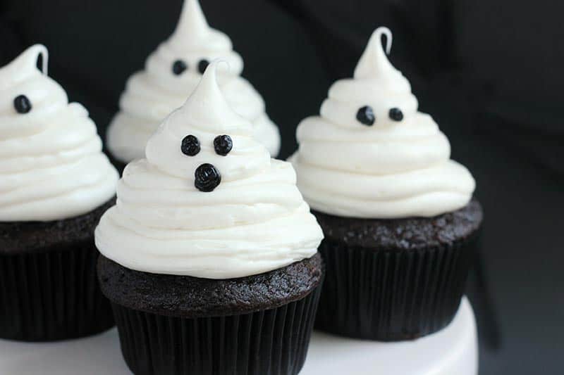 close up image of a white cake stand topped with frosted cupcakes that look like ghosts
