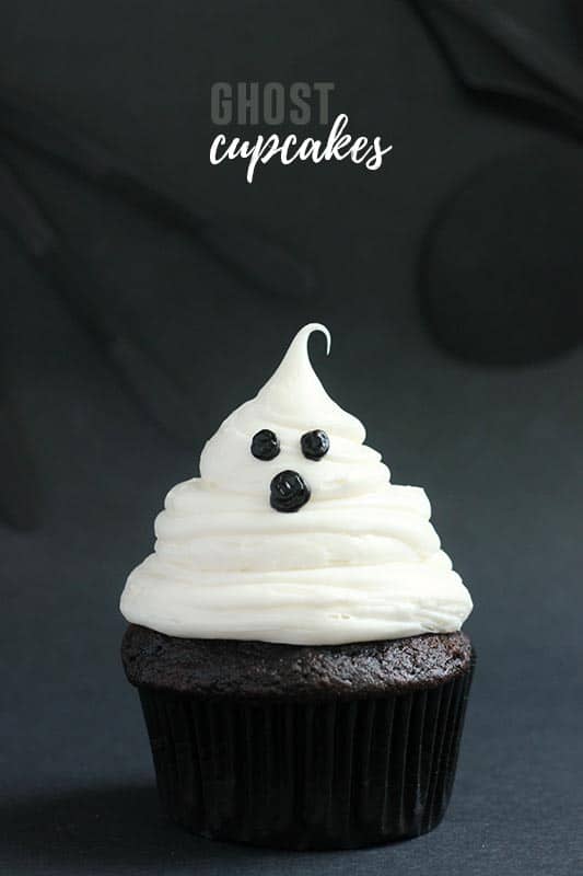single chocolate cupcake in a black wrapper topped with white frosting that is shaped like a ghost on a black backdrop