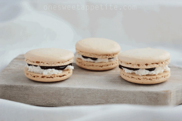 Three macarons sitting on a wooden plank filled with chocolate and marshmallow