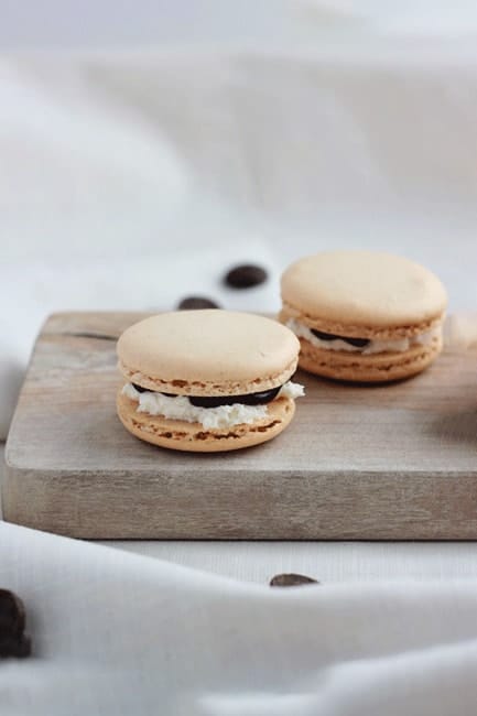 two French macaron cookies, filled with chocolate and marshmallow filling, sitting on a wooden plank