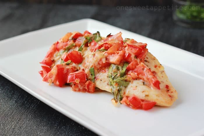 chicken breast that has been cooked and is topped with diced tomatoes and basil pieces sitting on top of a white plate
