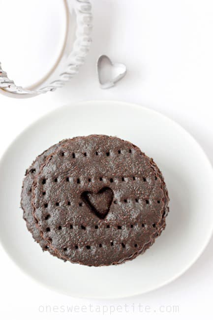 Top down image showing a stack of chocolate thin cookies that are sitting on a small white plate with cookie cutters off to the side
