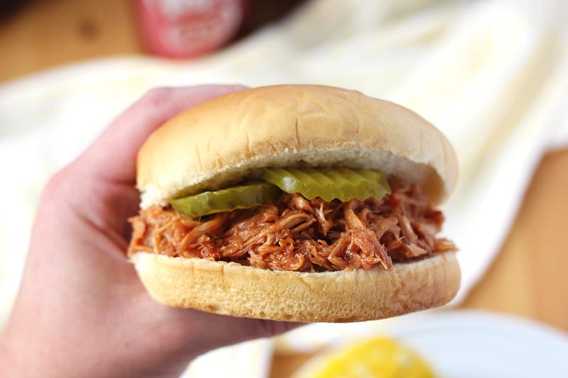 Sandwich with pulled pork and pickles held by a hand