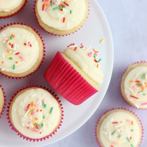 Overhead view of assorted frosted vanilla cupcakes topped with sprinkles on a plate.