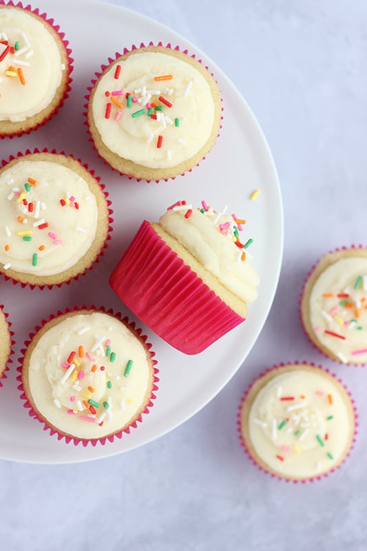 Overhead view of assorted frosted vanilla cupcakes topped with sprinkles on a plate.