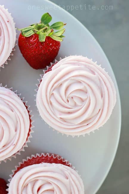 Top down shot of strawberry cake mix cupcakes sitting on a white cake plate with a fresh strawberry