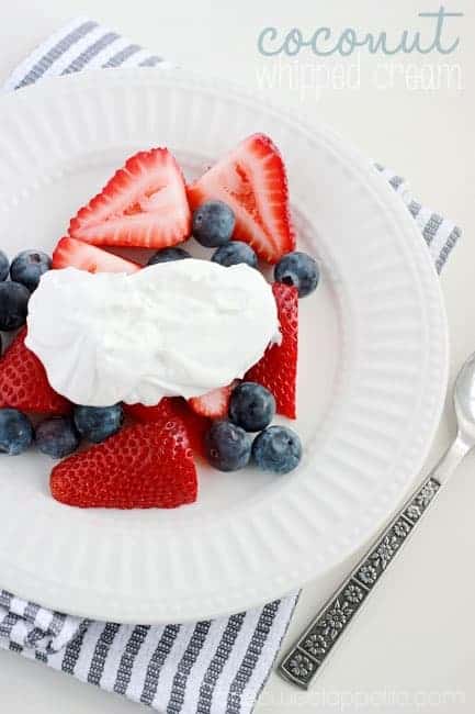 close up image of a white round plate that is topped with sliced strawberries and blueberries with a spoonful of whipped cream on top