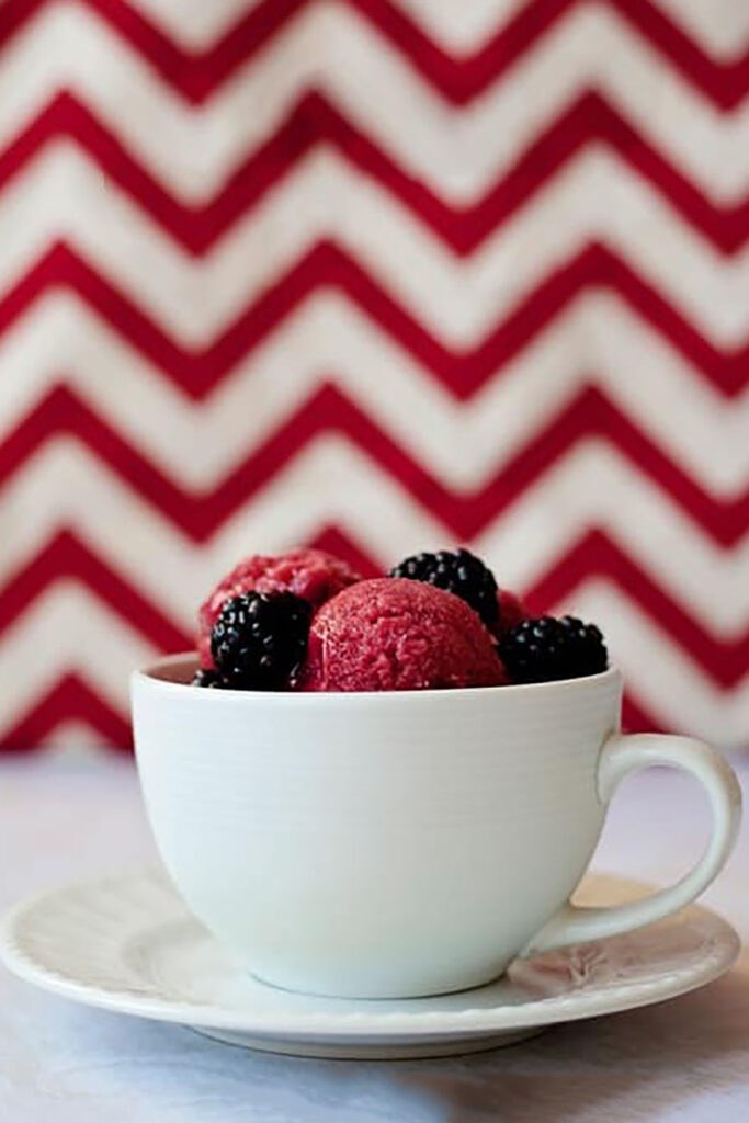 white mug sitting on a saucer filled with scoops of sorbet with fresh blackberries sitting on top