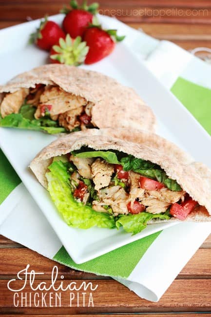 close up image of a pita that is filled with chicken, tomatoes, and lettuce on a white rectangle plate