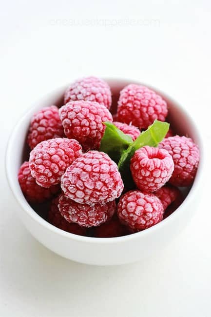 small white bowl filled with frozen raspberries and a mint sprig