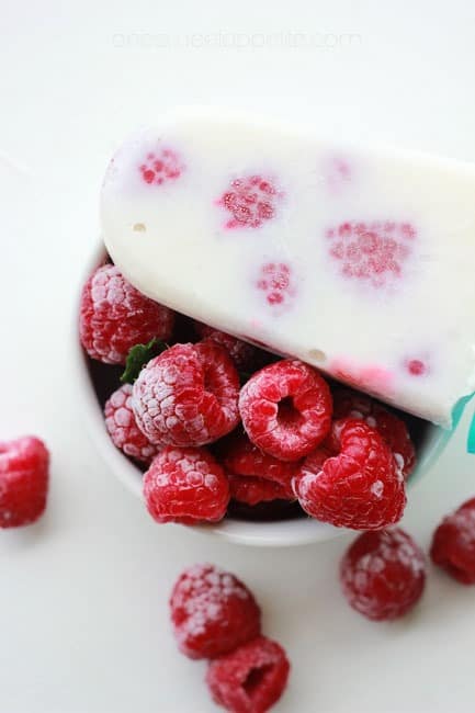 closs up image of a bowl of frozen berries with a white popsicle sitting off to the side of the bowl. 