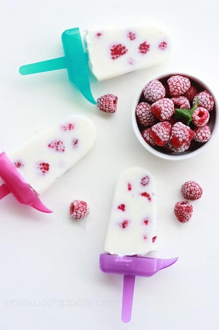 three popsicles sitting on a white table with frozen raspberries