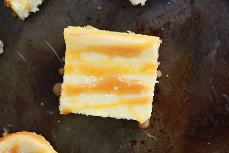 top down image showing a single cheesecake bar that has been drizzled with caramel sauce. The bar is sitting on a dark tin pan