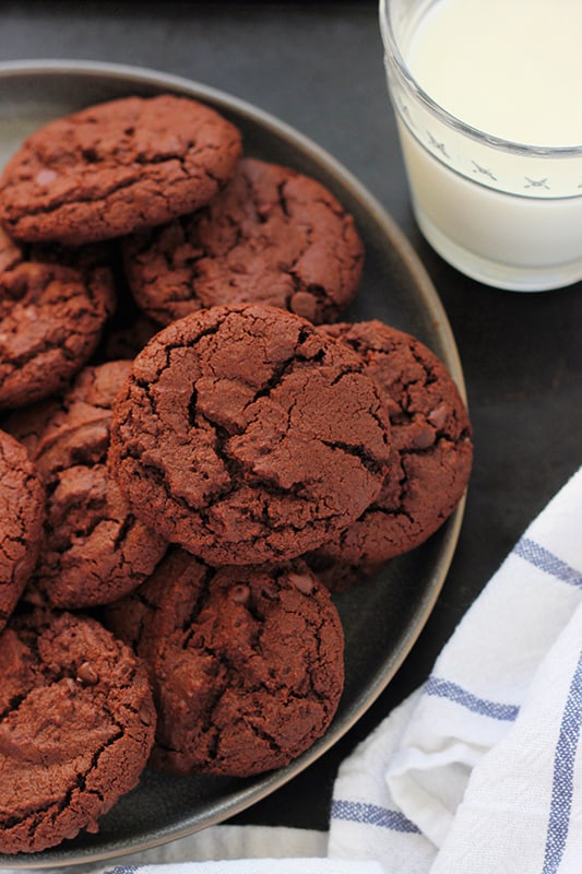Chocolate cookies stacked on a black plate with a glass of milk on the side