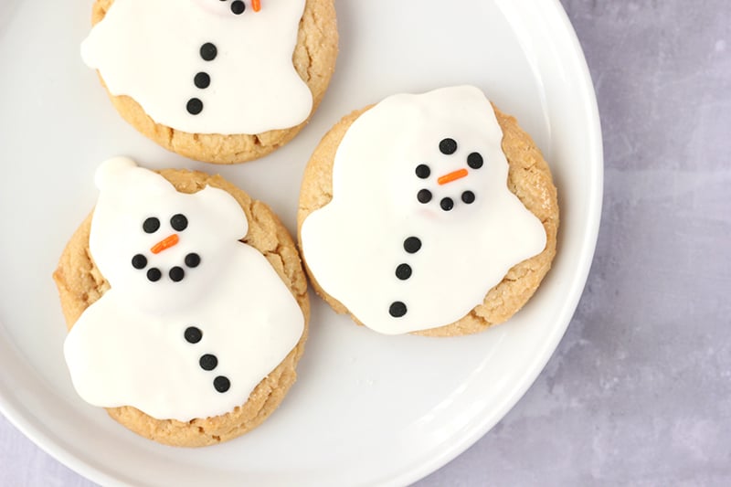 3 Melted Snowman Cookies on a white plate placed on the counter