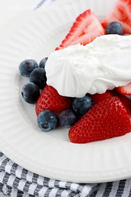 close up image of a white round plate that is topped with sliced strawberries and blueberries with a spoonful of whipped cream on top