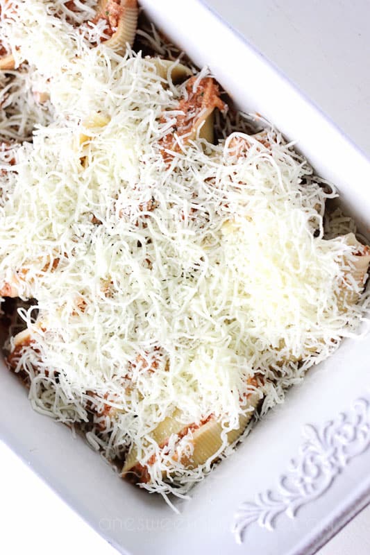 White baking dish that is filled with stuffed shells and smothered in shredded mozzarella cheese on a white backdrop