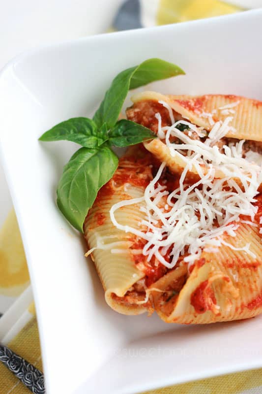 three pasta shells in a white bowl sprinkled with extra cheese and a side of fresh basil