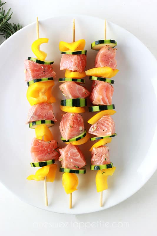 uncooked skewers lined with salmon and vegetables on a white plate