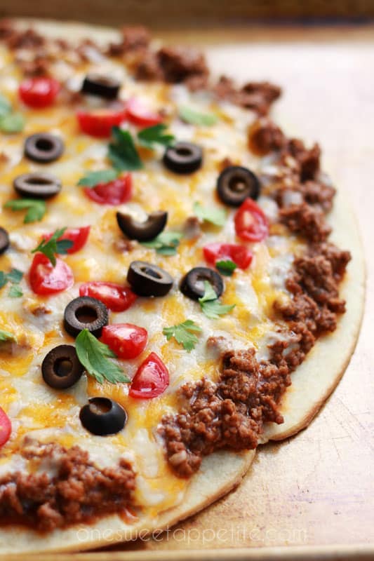 close up image of a pizza that is topped with ground beef, cheese, olives, tomatoes, and cilantro on a baking tray