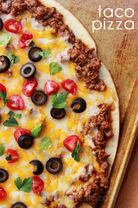 top down close up image of a pizza that is topped with ground beef, cheese, olives, tomatoes, and cilantro on a baking tray